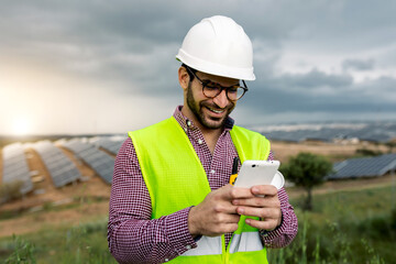 Happy engineer using smartphone near solar power plant