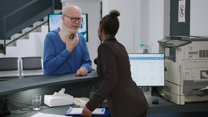 Medical worker helping injured patient with cervical collar at hospital reception counter, waiting to attend appointment with medic. Old man with neck brace in pain at health center.