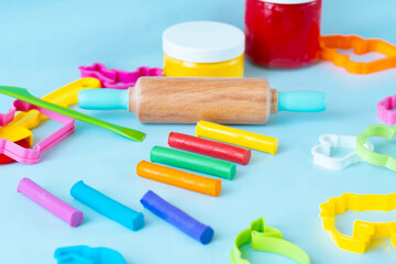 Colorful sticks plasticine with cutters, knife and roller on a blue background, multicolored modeling clay.