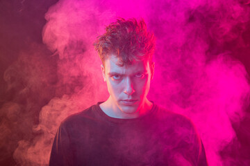 Smoke enveloped young man. Model looking at camera isolated over magenta background with clouds of smoke. Concept of mental health, art, emotions