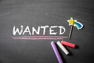 Wanted. Text and colored pieces of chalk on a dark blackboard