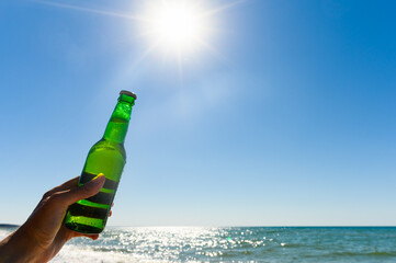 a bottle of cold beer in a hand against the backdrop of the bright rays of the sun. The concept of...
