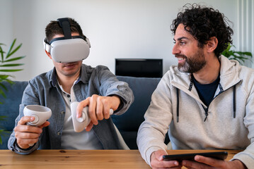 Caucasian men enjoying virtual reality glasses while sitting at table in home.