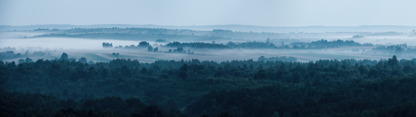 Country landscape morning mist in summer over fields and forests in hilly area from high angle view panoramic view