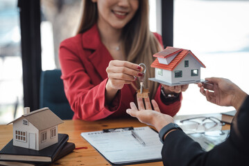 Real estate agent hand over the house key to customers after signing a real estate sales contract,...