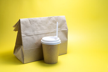 The concept of a quick snack and food delivery, a paper bag with food and a paper cup on a yellow background