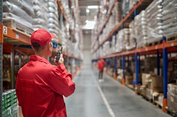 Warehouse worker communicating with his colleague over the walkie-talkie - obrazy, fototapety, plakaty