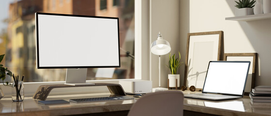 Modern office desk workspace with computer and laptop mockup on table against the window.
