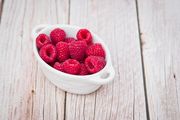 Harvest of Fresh ripe farm raspberry on the table, on wooden background in white plate. Top view, copy space. Flat lay with space for text.