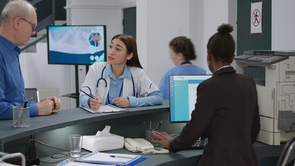 Asian doctor talking to senior patient at hospital reception desk, using report papers to fill in before attending medical appointment. Medic helping old man with consultation insurance.
