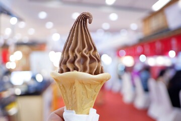A cone of chocolate Ice cream on a female hand with blurred inside a mall and bokeh light