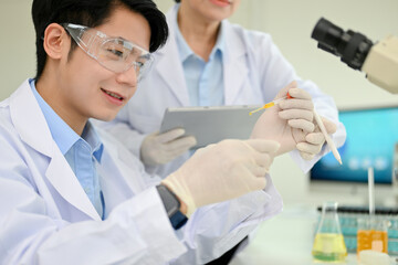 Smart Asian male scientist adjusts a virus sample in a Petri dish in his science lab.