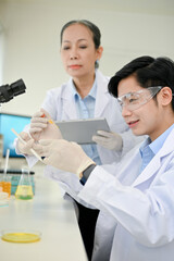 Professional Asian-aged female scientist instructs her young male scientist in the lab.