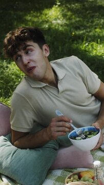 a young white man enjoying a healthy salad at a picnic in the park