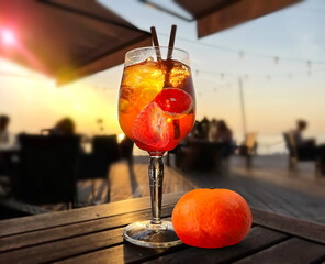 glass of fruit water  aperol  and mandarin on wooden  table on beach cafe at sunset on sea