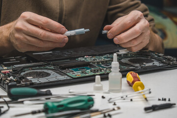 cleaning and replacing the old thermal paste with a new one on the laptop graphics card chip. a laptop repair and maintenance technician opens a tube of thermal paste for its application. close-up.