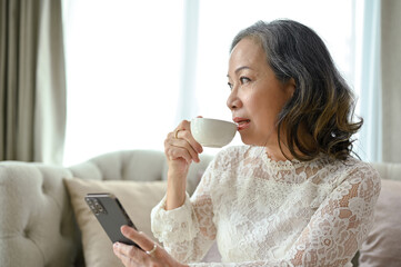 An attractive Asian middle-aged woman is sipping coffee while relaxing in the living room.