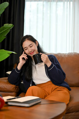 Pretty Asian female relaxes while sipping coffee and talking on the phone in the living room.
