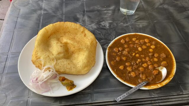 Top shot of Indian breakfast cuisine Chole Bhature or Poori with chickpea chana masala curry, served with mixed pickle and sliced onion.