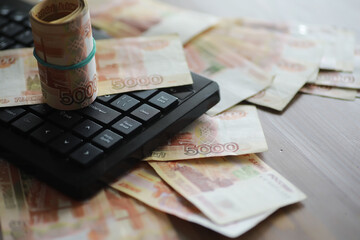 Stacks of 5000 ruble banknotes on the table next to the laptop. Savings and investments in the conditions of sanctions and inflation.