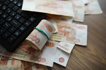 Stacks of 5000 ruble banknotes on the table next to the laptop. Savings and investments in the conditions of sanctions and inflation.