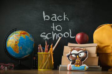 School supplies next to the globe and stack of books on the blackboard background. Back to school concept on September day