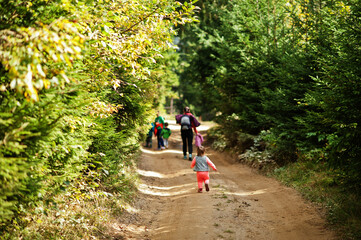 Obraz premium Mother with four kids resting in mountains. Family travel and hiking with childrens. Back of running baby girl.