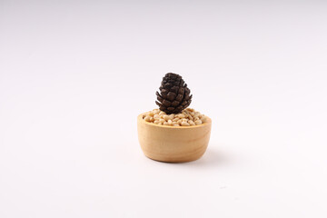 Heap of pine nuts and wood cup and cedar cones on white background
