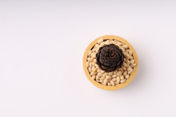 Heap of pine nuts and wood cup and cedar cones on white background