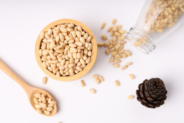 Heap of pine nuts and wood cup wood spoon and cedar cones on white background