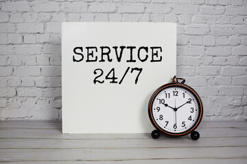 24/7 Service alphabet letters and alarm clock on white brick wall background
