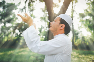 Religious muslim man  traditional kandura praying  outdoor at quiet nature  environment sun beams.
