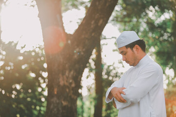 Religious muslim man  traditional kandura praying  outdoor at quiet nature  environment sun beams.