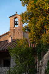 Fototapeta na wymiar Church tower of a small chapel in Vallon Pont d’Arc village in southern France. Sunset atmosphere with warm evening light illuminating the bell tower in typical architecture of rural Provence region.