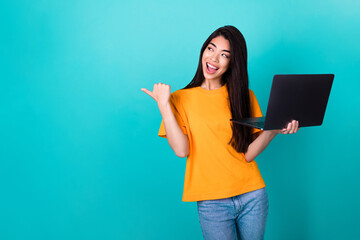 Photo of impressed millennial lady index empty space hold laptop wear orange t-shirt isolated on turquoise color background