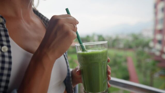 Young smiling woman drinking detox smoothie through straw. Happy vegetarian drinks fresh green vegetable cocktail. Weight Loss, slimming Concept. Healthy eating habits. High quality 4k footage