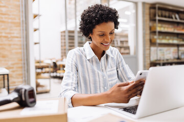 Cheerful online store manager reading a text message on her smartphone