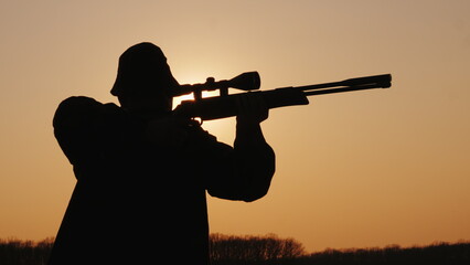 A man with a rifle takes aim at sunset, silhouette