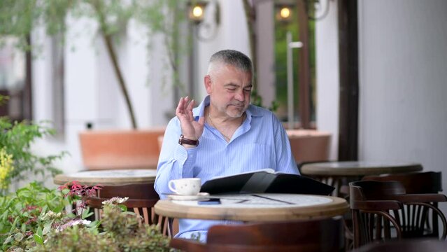 Handsome caucasian middle aged man hoosing lunch menu in street cafe.