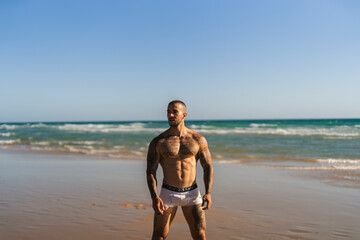 Fototapeta na wymiar Chico joven tatuado y musculoso en bañador y ropa interior en la playa