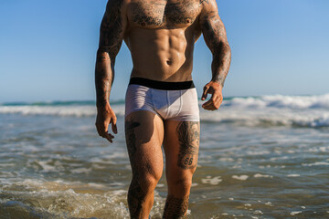 Chico joven tatuado y musculoso en bañador y ropa interior en la playa