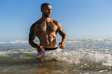 Chico joven tatuado y musculoso en bañador y ropa interior en la playa
