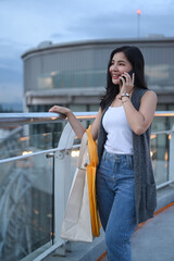 Attractive asian woman with shopping bags standing on terrace of modern building overlooking the city. Lifestyle concept