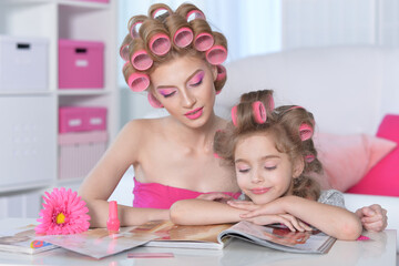 Obraz na płótnie Canvas Mother and little daughter with hair curlers reading magazine