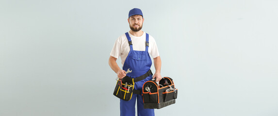 Handsome worker with tools bag on light background