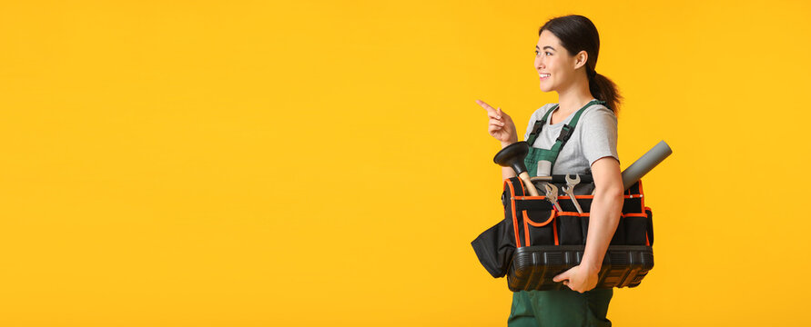 Female plumber with tools bag pointing at something on yellow background with space for text