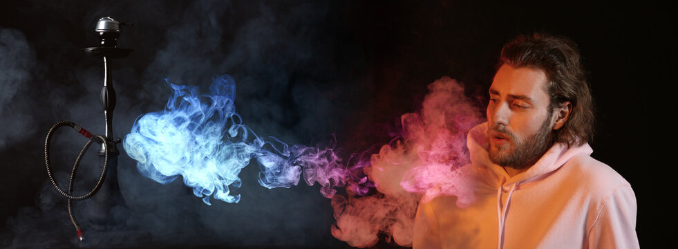 Young man smoking hookah on dark background