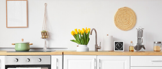 Modern electric stove with sink, tulip flowers and utensils in light kitchen