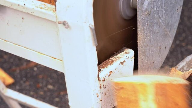 Closeup of crosscut saw blade cutting firewood from wooden pine planks - Wood slowly pushed towards saw before falling down on other side