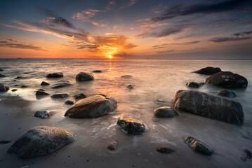 Morze bałtyckie - wschód słońca na plaży z widokiem na fale i kamieniste wybrzeże bałtyku, koło klifu w Gdynia Orłowo - obrazy, fototapety, plakaty